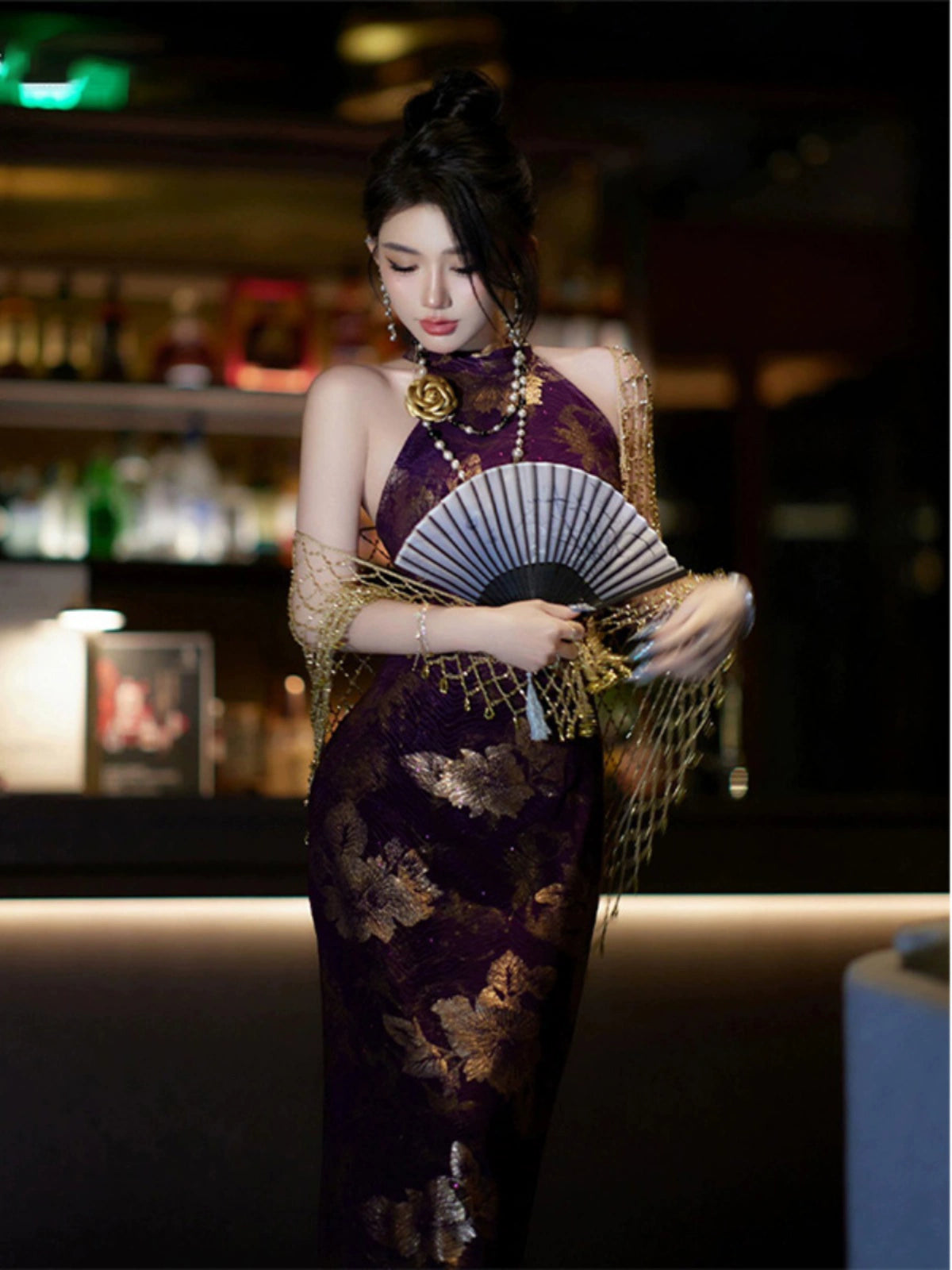 Purple jacquard cheongsam dress with halter neckline and gold floral patterns, accessorized with a fan and gold shawl for evening elegance.