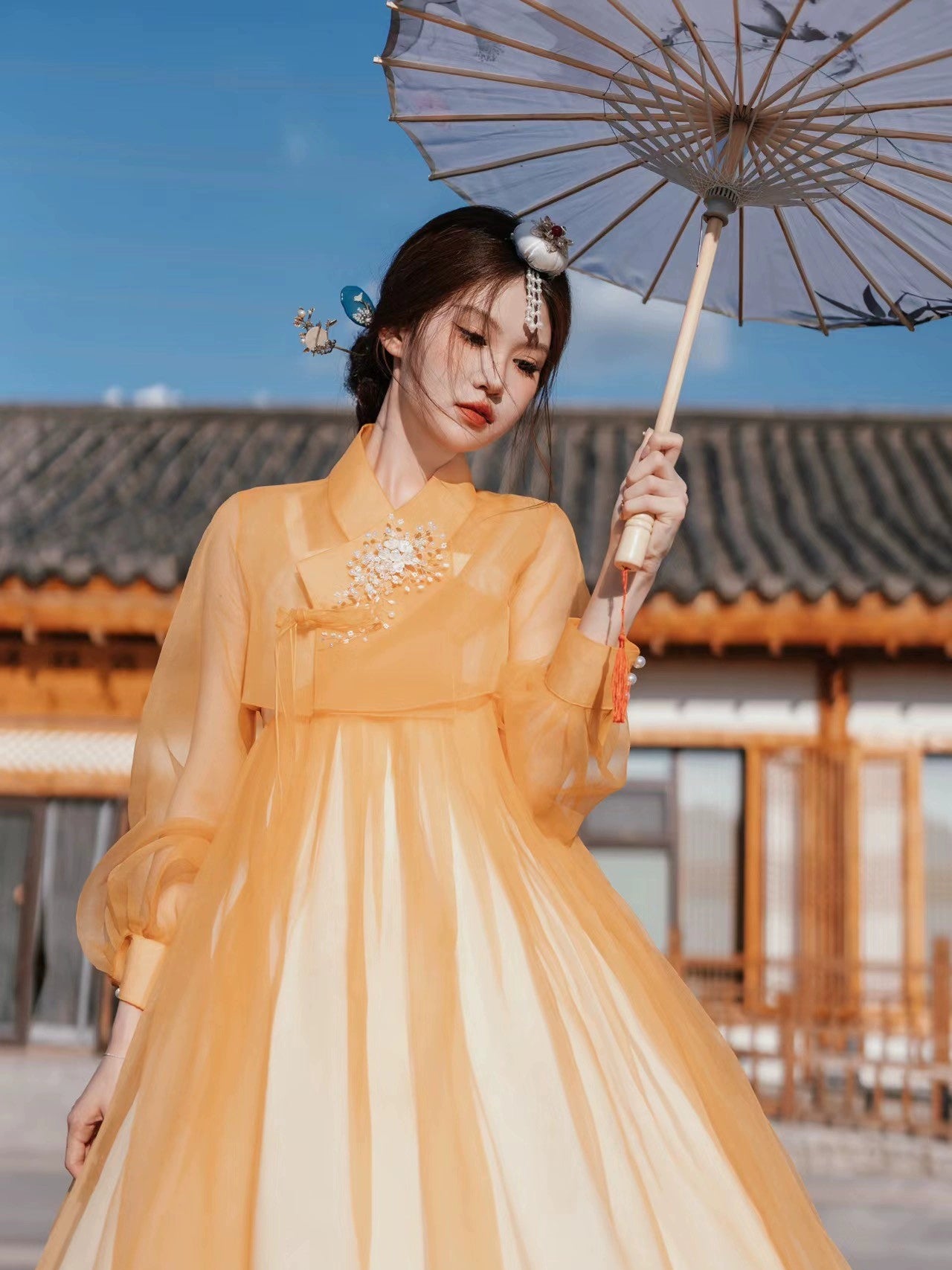 Elegant orange Yanbian Yanji Korean Hanbok dress with delicate embroidery, worn by a woman holding a traditional parasol in a historical courtyard.