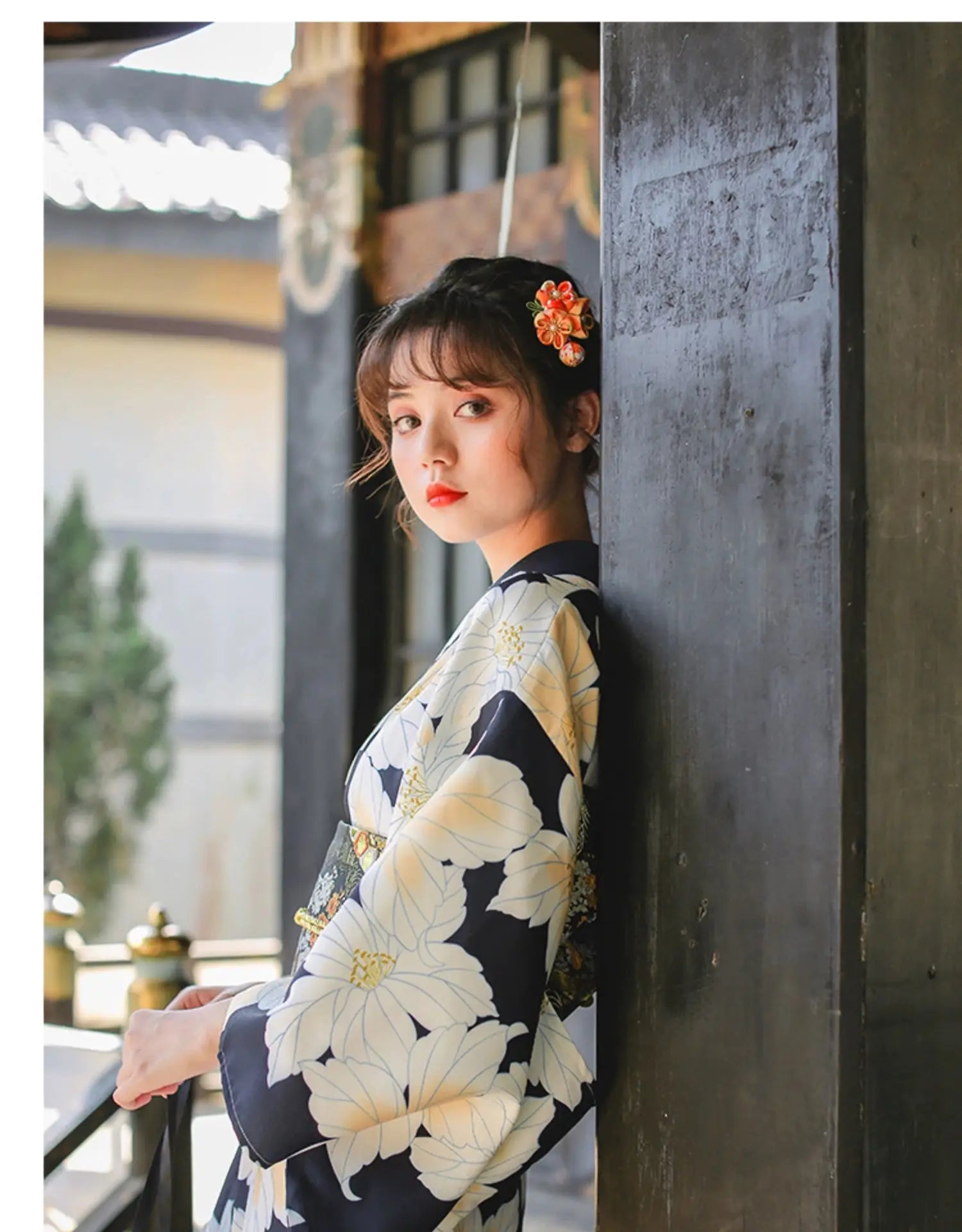 Woman leaning against a pillar in a Japanese kimono dress, featuring a black and white floral design and elegant obi belt.