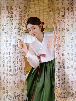 Charming green hanbok with floral accents, showcased behind Korean script curtains.