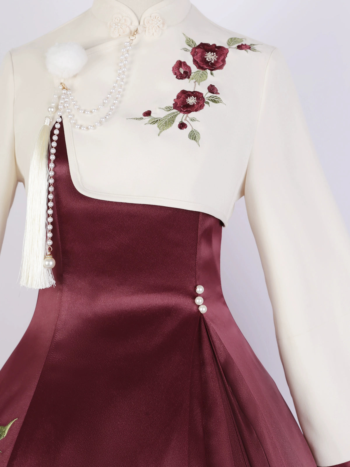 Close-up of cream top and burgundy skirt with floral embroidery and pearl tassel details from the Camellia Lolita cheongsam.