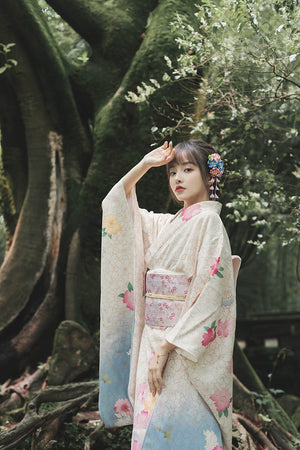 Model in a white floral kimono, standing elegantly in a lush forest environment.