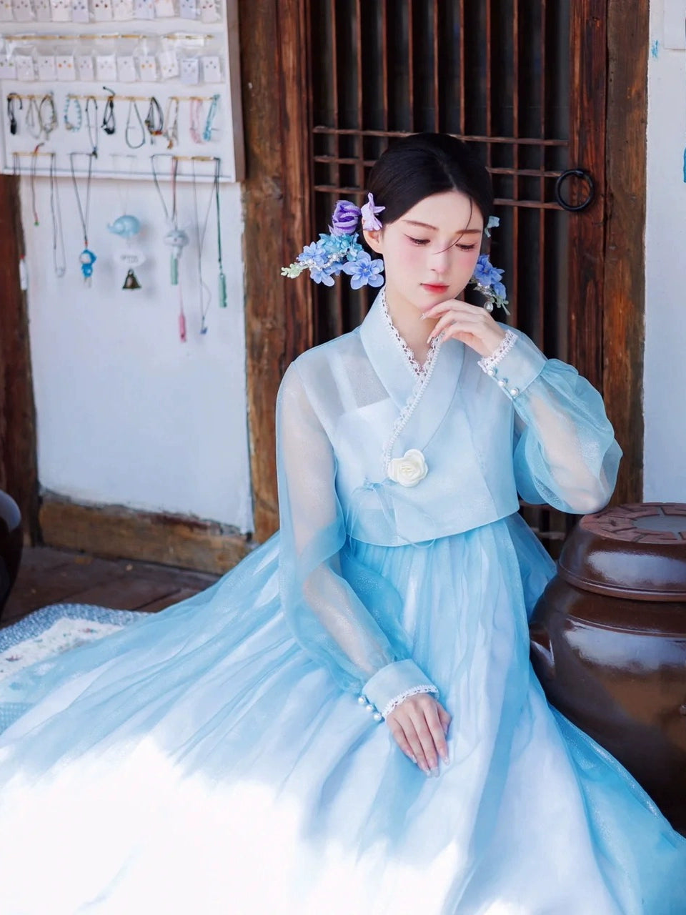 Graceful blue Hanbok dress with delicate floral embellishments, seated pose.