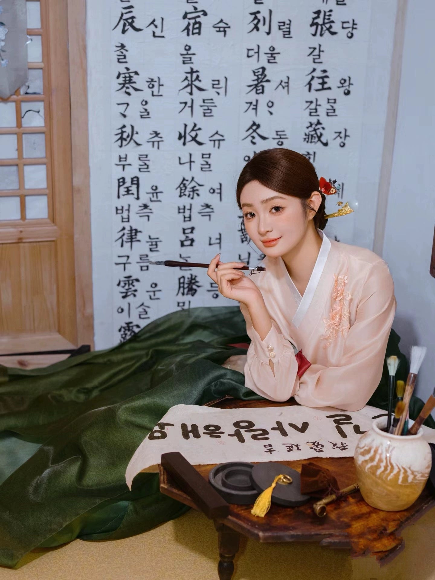 Cultural green hanbok with calligraphy tools in a traditional Korean room.