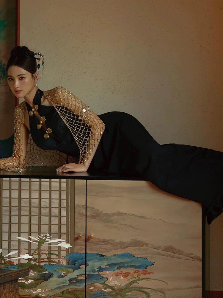 Retro black fishtail cheongsam dress styled with a gold beaded shawl, lying gracefully on a traditional cabinet.