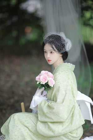 Model holding pink roses in a green kimono with white lace gloves.