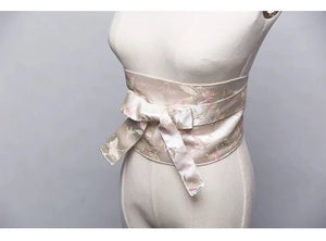 White brocade kimono belt seal with pink and green floral embroidery, tied in a bow and displayed on a mannequin for a refined look.