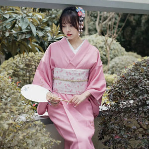 Pink Japanese kimono yukata with floral patterns, styled with a white obi and traditional hair accessories, perfect for photography and travel.