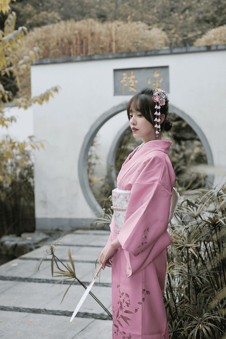 Pink Japanese kimono yukata with floral details, styled with a white obi and fan, photographed in front of a traditional circular gate.