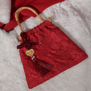 Red floral-patterned bridal handbag with bamboo handle and tassel detail, lying on a white and red background for wedding styling.