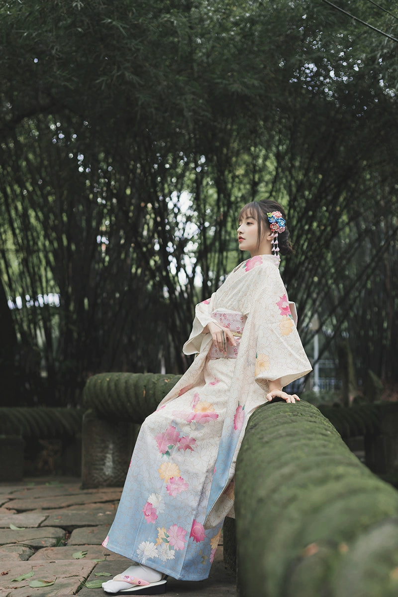 Elegant Japanese kimono with floral patterns, worn by a model sitting on a mossy bridge.