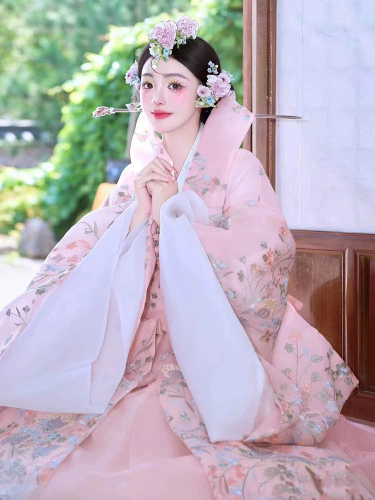 Traditional pink Korean court dress with floral patterns, seated gracefully.