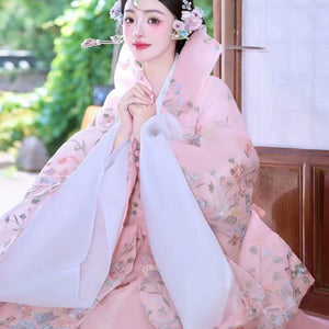 Pink Korean traditional dress with floral details, seated in a serene pose.