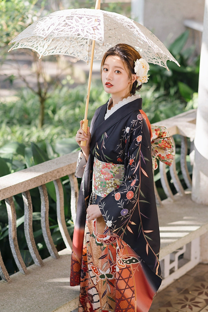 Model in a black kimono with butterfly and floral designs, holding a parasol.