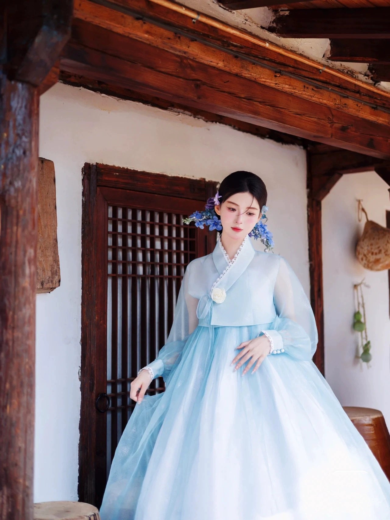 Elegant blue Hanbok Korean court dress with floral accents, worn outdoors.