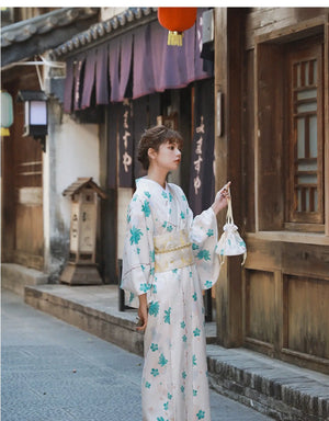 Woman in a white and blue floral Yukata Kimono Dress holding a matching bag, standing in front of traditional Japanese wooden architecture.