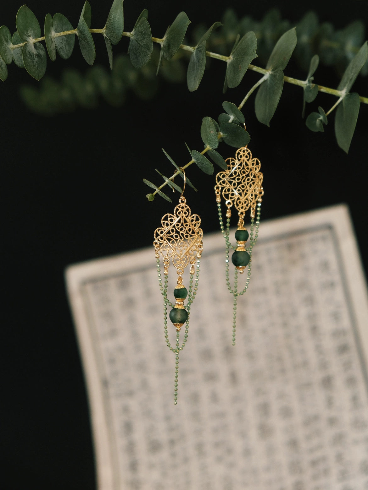 Su Mask Ear Clips - Hanfu Gold Tassel Earrings featuring intricate floral design and green beads, styled with Chinese calligraphy backdrop.