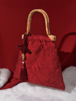 Elegant red bridal handbag with floral textured fabric, bamboo handle, and decorative tassel. Perfect for weddings and special events.