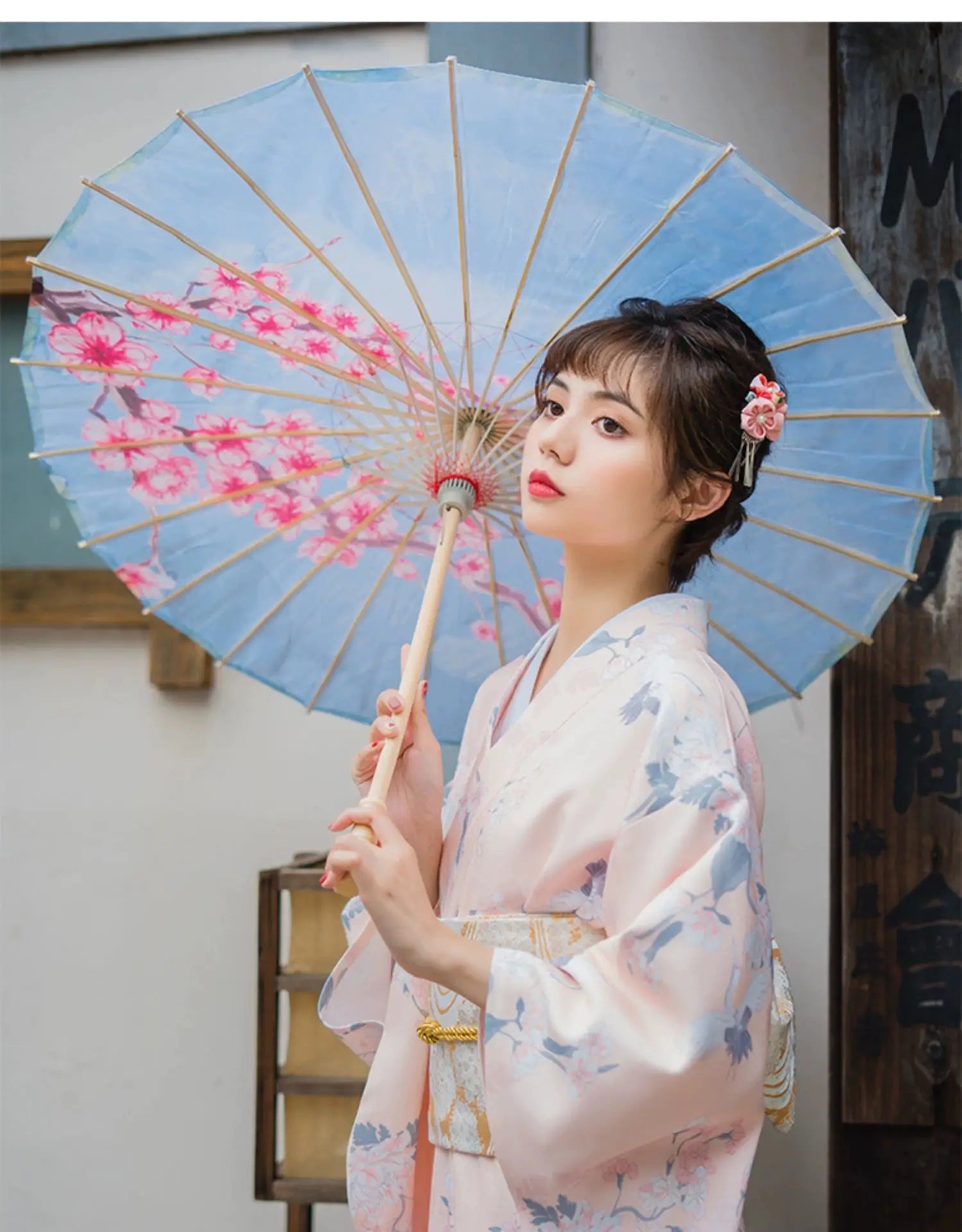 Woman in a pink crane-patterned yukata kimono, holding a parasol with cherry blossom design, embodying a retro Japanese aesthetic.