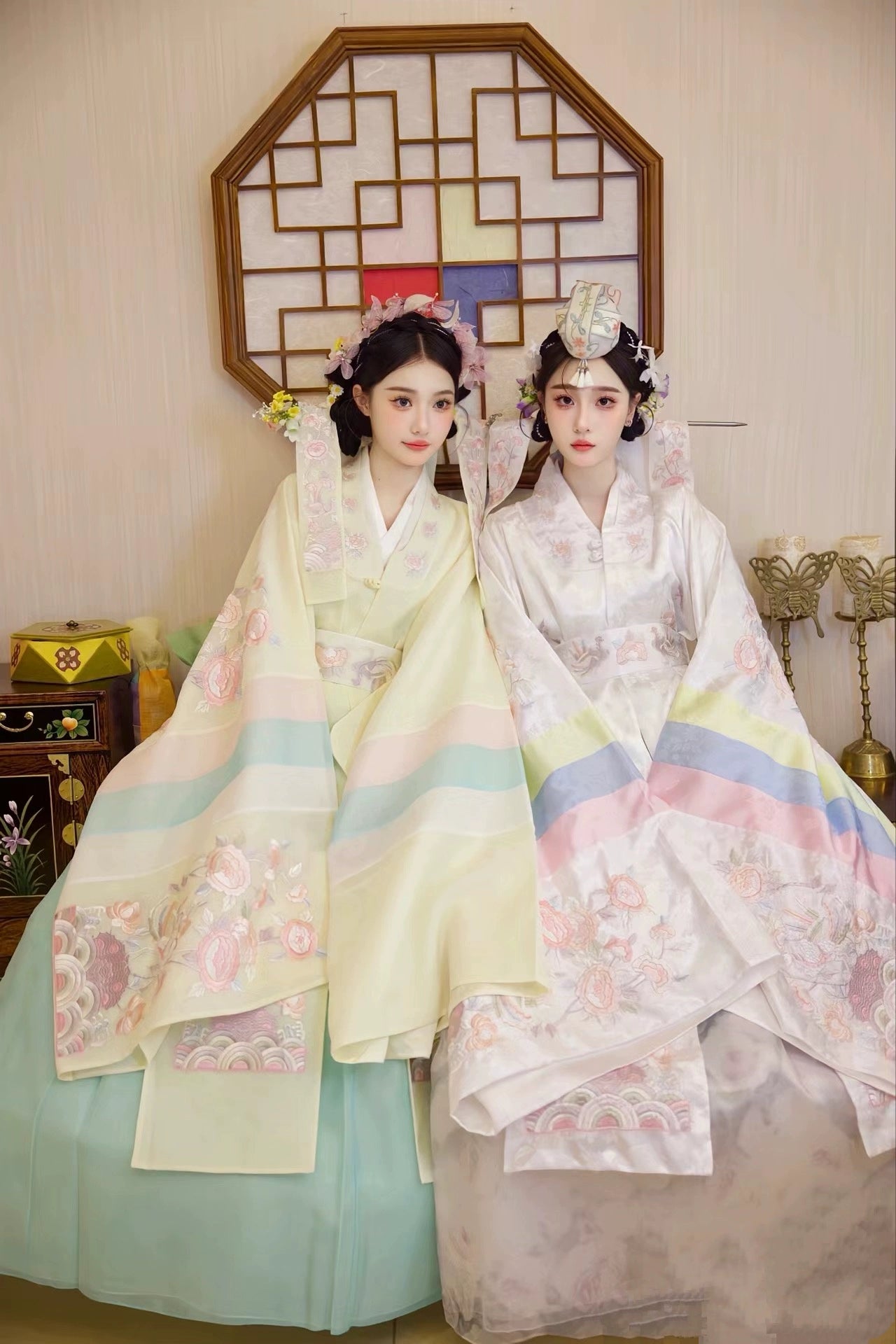 Two brides in Muzhi Korean embroidered wedding dresses, one in white and the other in soft yellow, showcasing intricate floral patterns and pastel details.