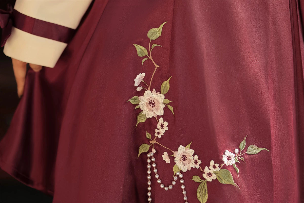 Detailed view of burgundy skirt with floral embroidery and pearl tassel embellishments from the Camellia Lolita cheongsam.