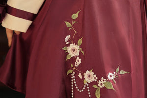 Detailed view of burgundy skirt with floral embroidery and pearl tassel embellishments from the Camellia Lolita cheongsam.