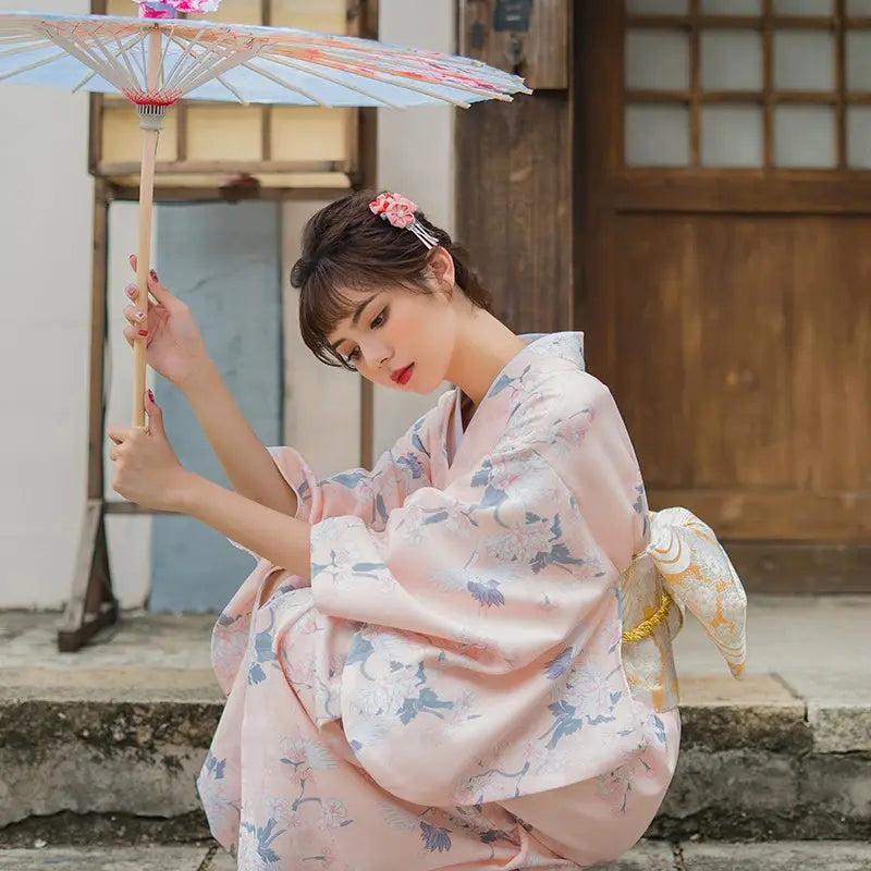 Woman wearing a retro pink yukata kimono with crane and floral patterns, holding a parasol, showcasing a gentle literary Japanese style.