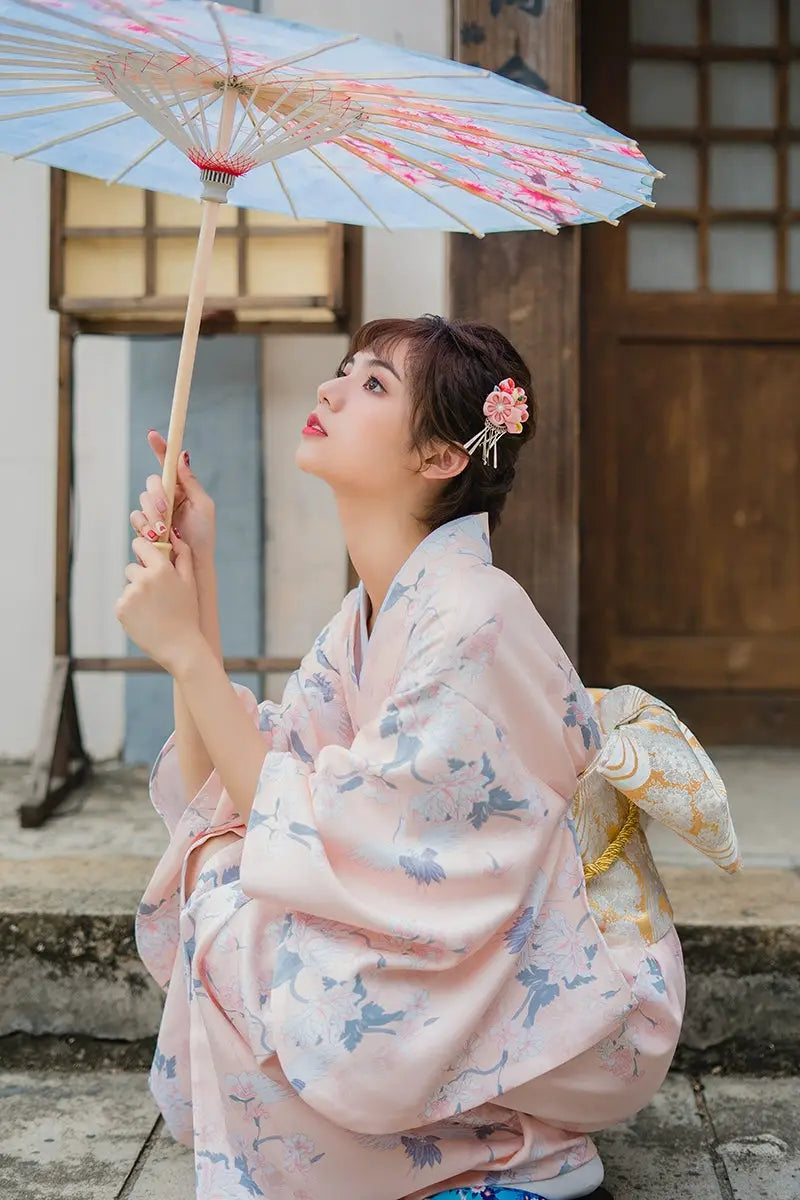 Close-up of a woman in a pink crane-patterned yukata kimono, holding a parasol, embodying a retro Japanese aesthetic.