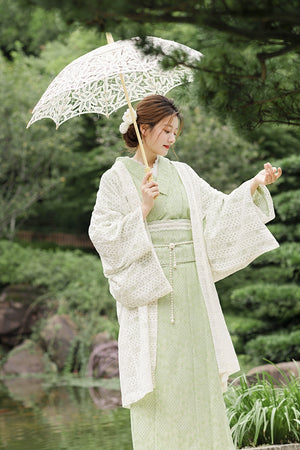 Model in green kimono dress holding lace parasol by a pond.