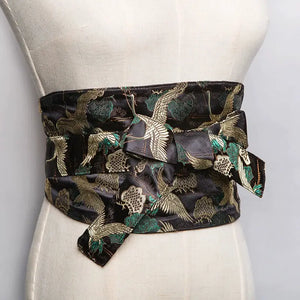 Black brocade kimono belt seal with intricate crane and floral patterns in gold and green, styled on a mannequin for a Japanese aesthetic.