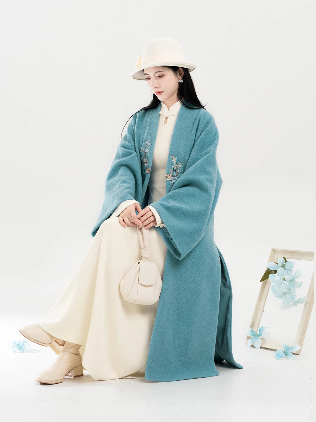 Teal floral coat and ivory dress in a seated pose