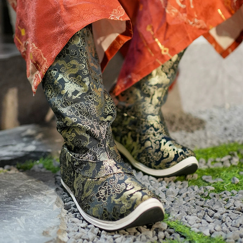 Detailed view of embroidered Dragon boots in black and gold, paired with a red Hanfu robe, showcasing Ming-dynasty inspired footwear.