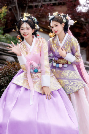 Pink and purple Hanbok with intricate gold patterns, worn by two women in a traditional setting.