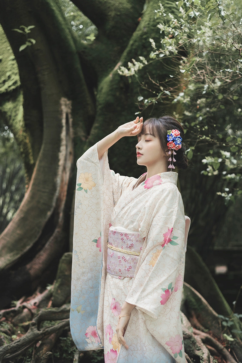 Woman in a white Japanese kimono with pink flowers, posing gracefully under a tree.