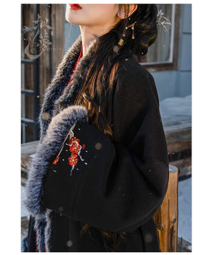 Close-up of black woolen Hanfu coat with floral embroidery and soft faux fur cuffs, paired with a red pleated skirt for winter.