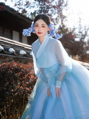 Blue Hanbok Korean dress with flowing design, worn in a scenic outdoor setting.