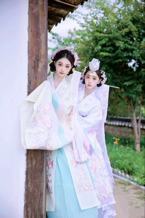 Traditional Korean wedding dresses by Muzhi in white and soft yellow, adorned with intricate embroidery and pastel accents for an elegant bridal ensemble.