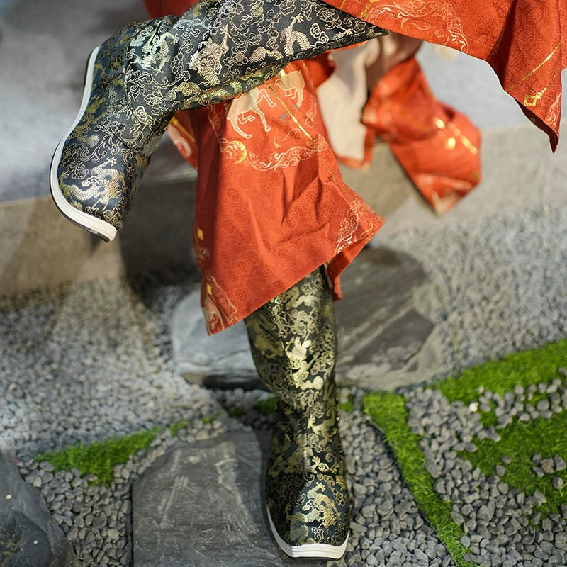 Black and gold embroidered Dragon boots styled with a red Hanfu robe, displayed on stone pavement with green moss accents.