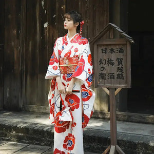 Women's white and red Japanese kimono dress with floral patterns, featuring wide sleeves and a traditional obi belt, styled in an outdoor setting.