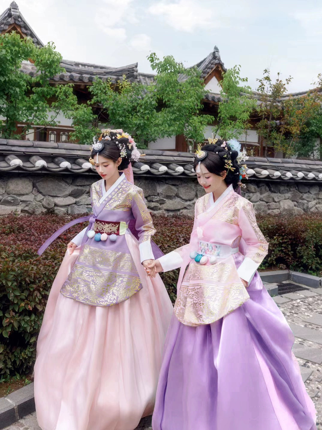 Two women walking in pink and purple Hanbok, showcasing traditional Korean elegance.