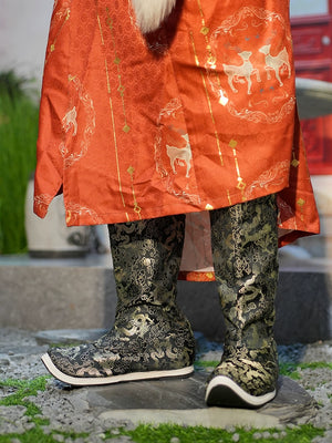 Close-up of intricately embroidered Dragon boots in black and gold, styled with a traditional red Hanfu robe on stone pavement.