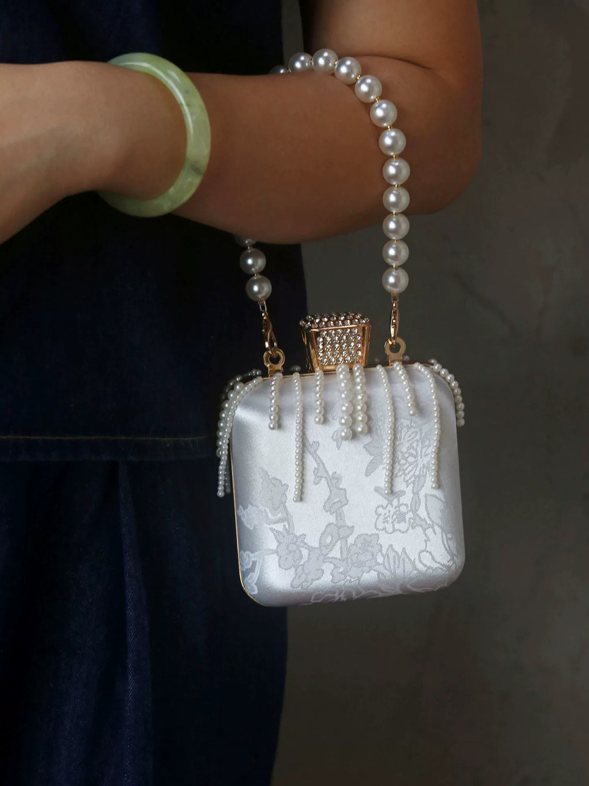 White pearl-style handbag worn at the wrist