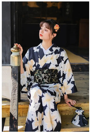 Woman in a navy floral yukata paired with a black brocade kimono belt seal, sitting gracefully with a matching floral hair accessory.