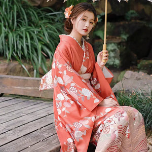 Elegant orange kimono with chrysanthemum motifs, styled with a lace parasol and floral hair accessory for travel photography.