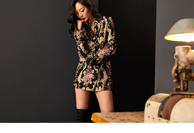 Model posing in black and gold jacquard dress suit with floral design.