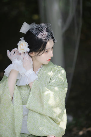 Model adjusting hairpiece in green lace kimono dress.