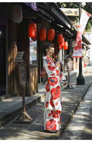 Woman in a white and red floral Japanese kimono dress, seated outdoors with a thoughtful pose, showcasing the intricate design.