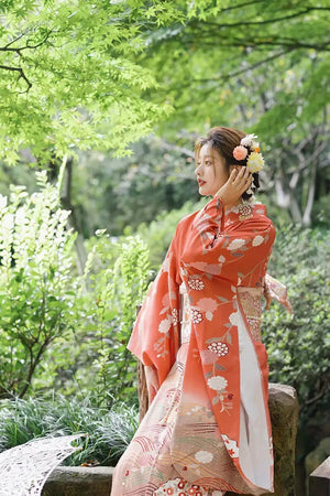 Elegant orange kimono with chrysanthemum patterns, styled with floral hair accessories, perfect for photography in a natural setting.