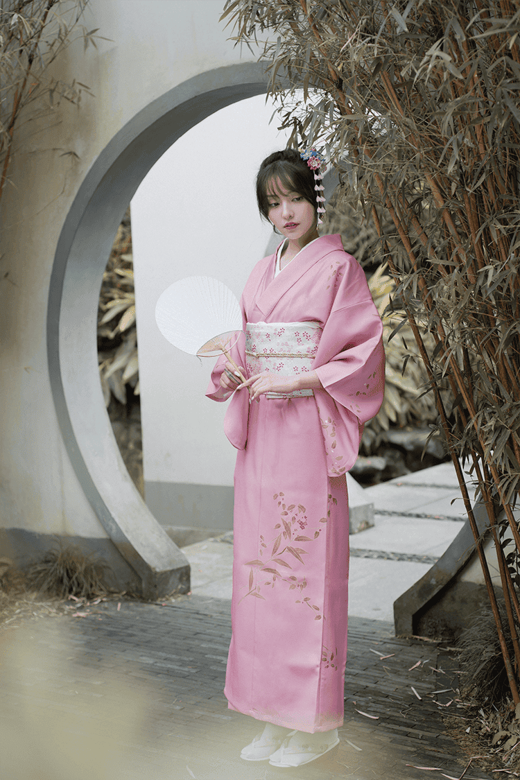 Elegant pink Japanese kimono yukata with floral designs, styled with a white obi, captured in a bamboo garden setting.