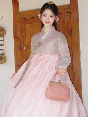 Woman in traditional Korean hanbok with a pink skirt and light blouse, holding a matching handbag.